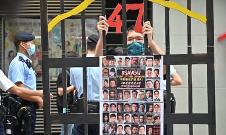 A protester stands behind a mock jail with photos of the 47 pro-democracy figures in May 2021