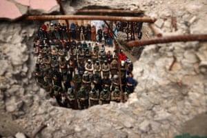 Rows of men praying are seen through a hole in a wall