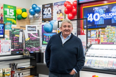 A large grey-haired man stands in front of a newsagent counter 