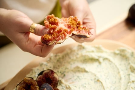 Hands tearing apart a ripe fig, over a platter of labneh.