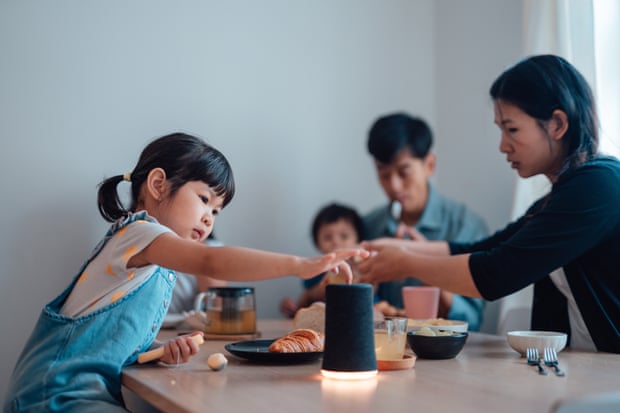 Curious young girl using smart speaker while having breakfast with her family.