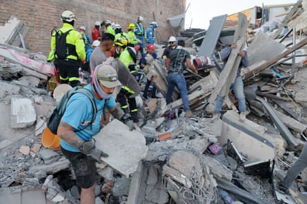 Rescuers, some in hi-vis jackets and hard hats clear remove pieces from a mountain of rubble