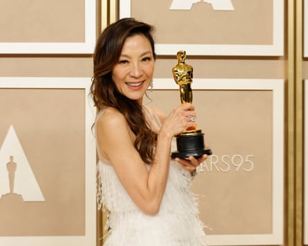 woman in white dress smiles with oscars trophy