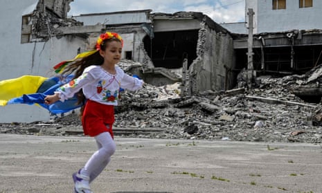 A child holding a Ukrainian flag runs past a cultural centre that was destroyed in a missile strike, during a graduation ceremony of art students in the town of Derhachi