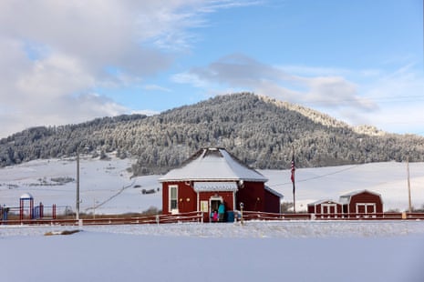 A snowy scene of a small, one-story, red, octagonal building, with a snowy, tree-covered mountainside beyond it.