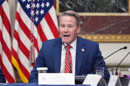 A man speaking at a desk in front of the US flag.