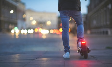 Man riding electric push scooter. Traffic street lights on background.
