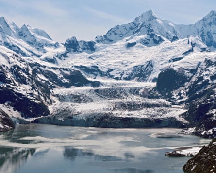 Johns Hopkins glacier in Alaska flows between snowy peaks into a calm, icy bay.