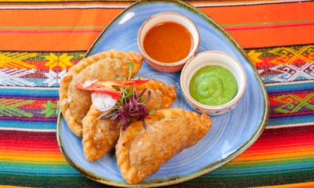 Vegetable empanadas with a green dip and a red dip, on a pale blue plate set on a colourful Mexican cloth
