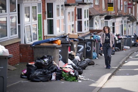 A man walks down a street with overflowing bins