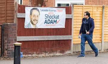 A man walking past an election campaign banner featuring an image of  independent candidate Shockat Adam