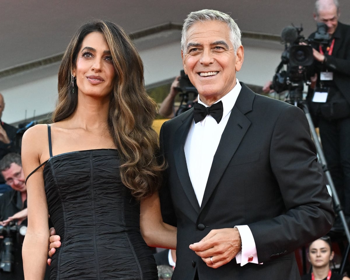 George Clooney and his wife, both clad in black pose for photographers on the red carpet.