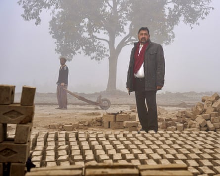 A man in a white shirt and black jacket stands next to rows of bricks drying on the ground.
