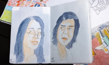 Two watercolour portraits in a sketchbook sitting on top of other sketchbooks.