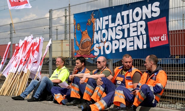 Workers sit in front of a banner reading “Stop the Inflation Monster” at the Burchardkai Container Terminal