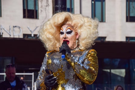 Peaches Christ speaking at the protest, wearing makeup, a shiny silver dress, black gloves and a big blond wig