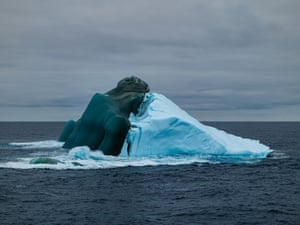 An iceberg that appears dark green on one side and light blue on the other