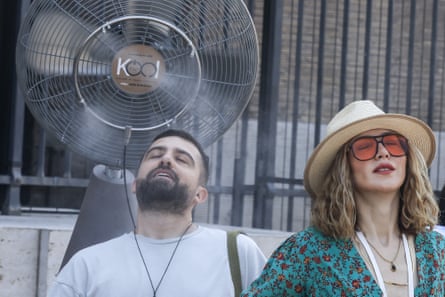 A man and a woman stand under the fan enjoying the water as it is sprayed on them