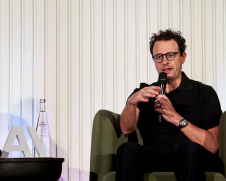 Dario Amodei speaks into a microphone while seated in a green chair on stage