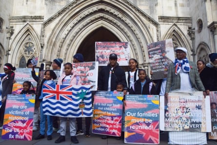 People stand in front of the court building entrance with signs that say: our families must be reunited
