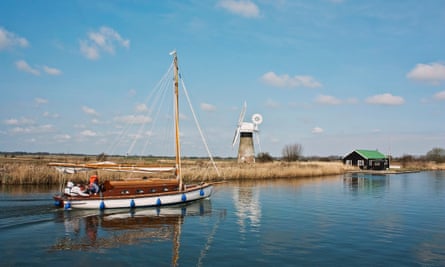A sail boat meanders along the Norfolk Broads at Thurne