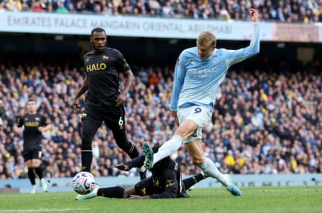 Erling Haaland kicks the ball past a sliding opponent, scoring a goal for Manchester City