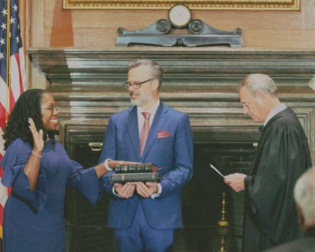 A smiling rests her hand on two Bibles held by a man wearing glasses, as a supreme court justice reads off a piece of paper in front of her