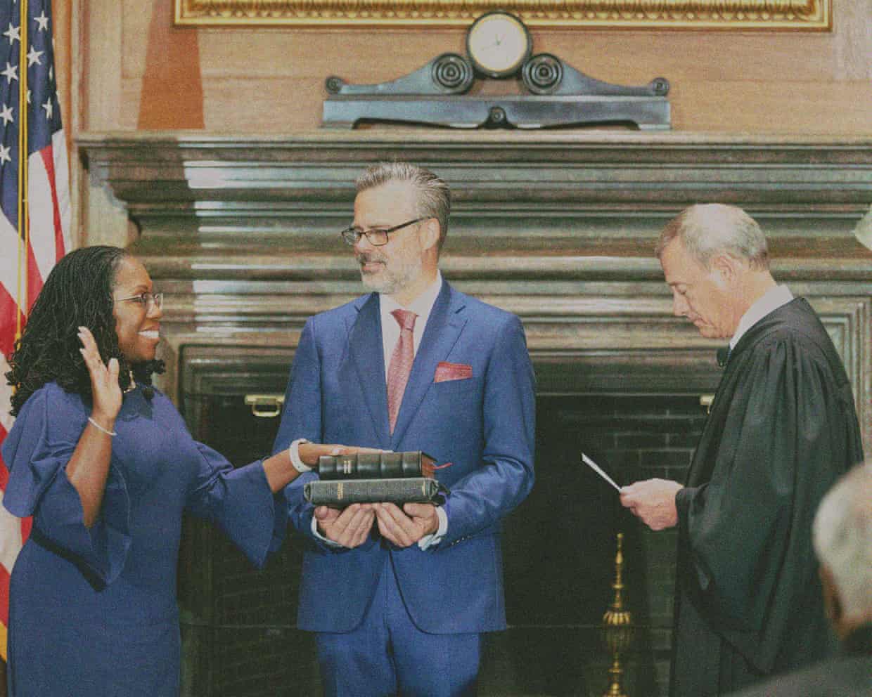 A smiling woman rests her hand on two Bibles held by a man wearing glasses, as a supreme court justice reads off a piece of paper in front of her