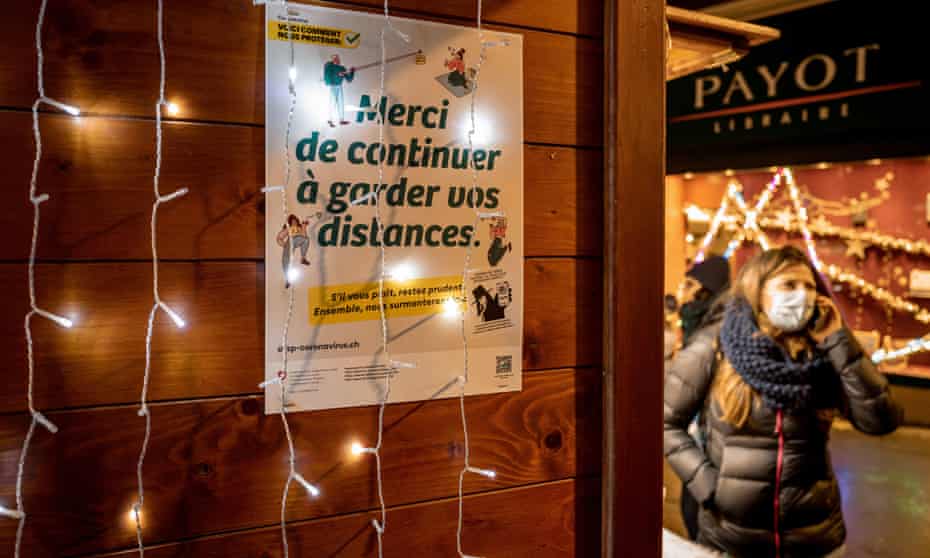 A woman walks past a sign reading in French: "Please continue to keep your distance" in a Christmas market in Lausanne on 2 December