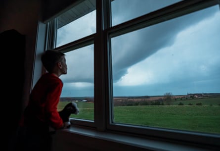 A boy with a toy dog watches dark storm clouds from a bedroom window.