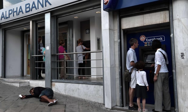 People withdraw cash from ATMs in central Athens on June 19, 2015, as a beggar lays on the pavement.