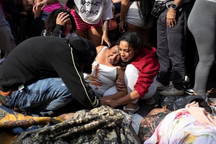 A woman cradles another woman crying over the body of her son.