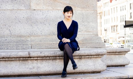 RF Kuang sits on a stone bench outdoors. She is wearing a dark blue dress