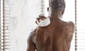 Unrecognizable Black Man Washing Back With Sponge Taking Refreshing Shower Standing Under Falling Hot Water In Modern Bathroom Indoors.