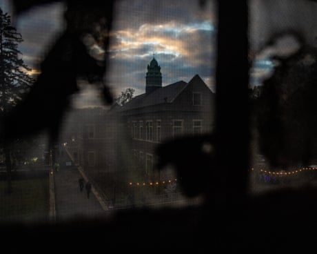 The Pennhurst Asylum building with a clock tower viewed through a dark, blurred foreground at dusk