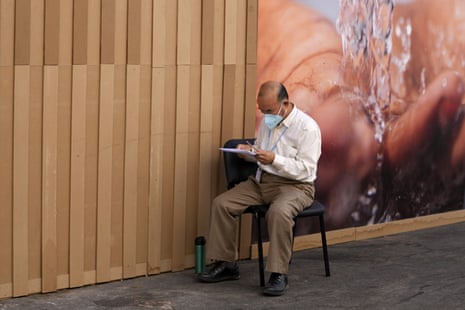 Sun Zhen reading a document, sitting sideways on a single chair against a wall.