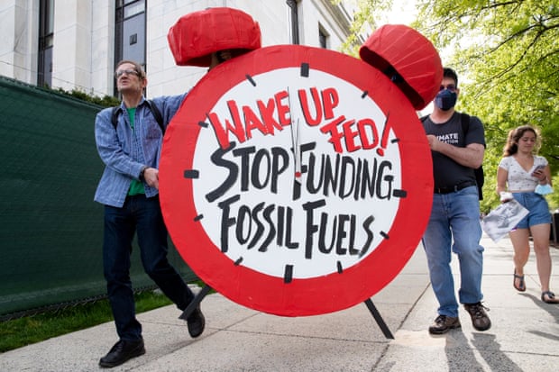 Activists carry a sign resembling a red alarm clock that reads 'Wake Up Fed!  Stop funding fossil fuels'.