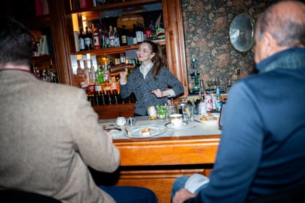 two men sit at the bar as a bartender shakes a cocktail shaker