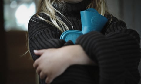 A close up of a young girl holding a hot water bottle and wearing a large jumper