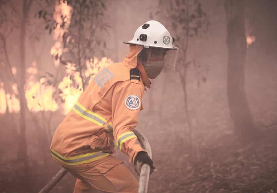 A man in fire suit pulling hose towards bushfire blaze
