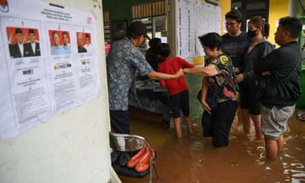 Electoral officers assist voters at a flooded polling station in Jelambar, West Jakarta