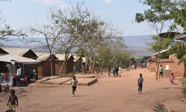 Refugee housing runs along a broad red dirt road.