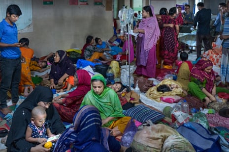 People lie on mattresses in a crowded corridor with drips on stands in the middle. Most of the people are children and women in colourful saris