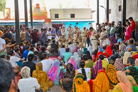 Seated police officers speak to a large crowd of men and women sitting on the ground