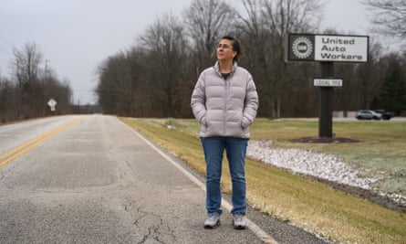 Sonja Woods, wearing a parka, jeans and trainers, stands on a road with her hands in her pocket in front of a sign reading “United Auto Workers”