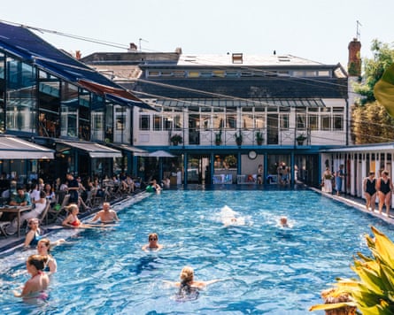 People swimming in a lido surrounded by buildings.