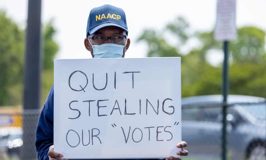 A man holds a sign saying 'Quit Stealing Our "Votes"'.