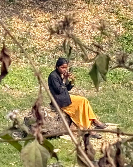 Monsumi Murmu sits alone on a tree trunk in the forest near her home.