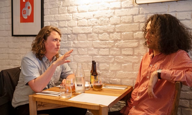 Dining across the divide: ‘He supports a new Heathrow runway – we should invest in trains’ 2 Jasper and Miles sitting at a restaurant table against a white-painted brick wall