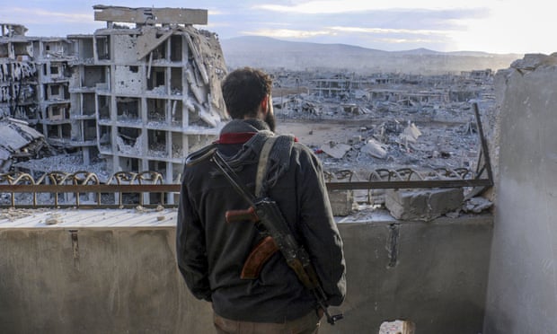 An armed Syrian surveys the wreckage of collapsed buildings in Daraya, Damascus.